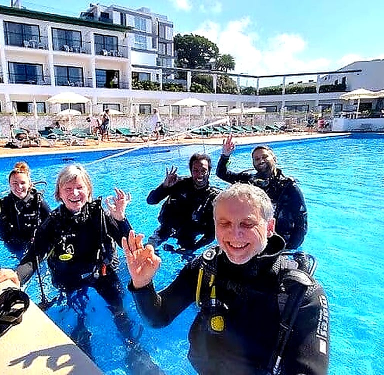 Happy group giving OK sign during try scuba diving experience at Quinta da Penha de França Mar pool, Madeira
