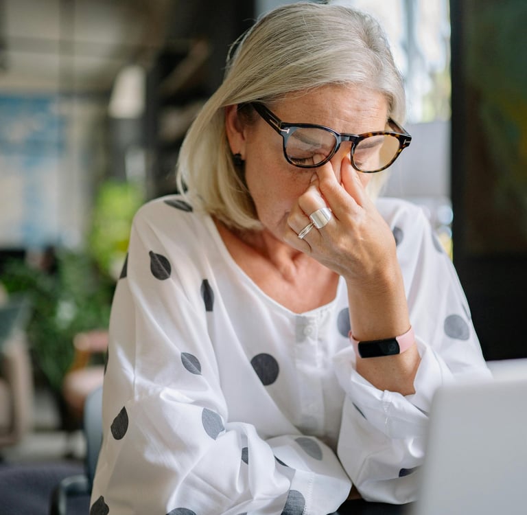 Anxious woman sits at her computer rubbing her eyes with tension