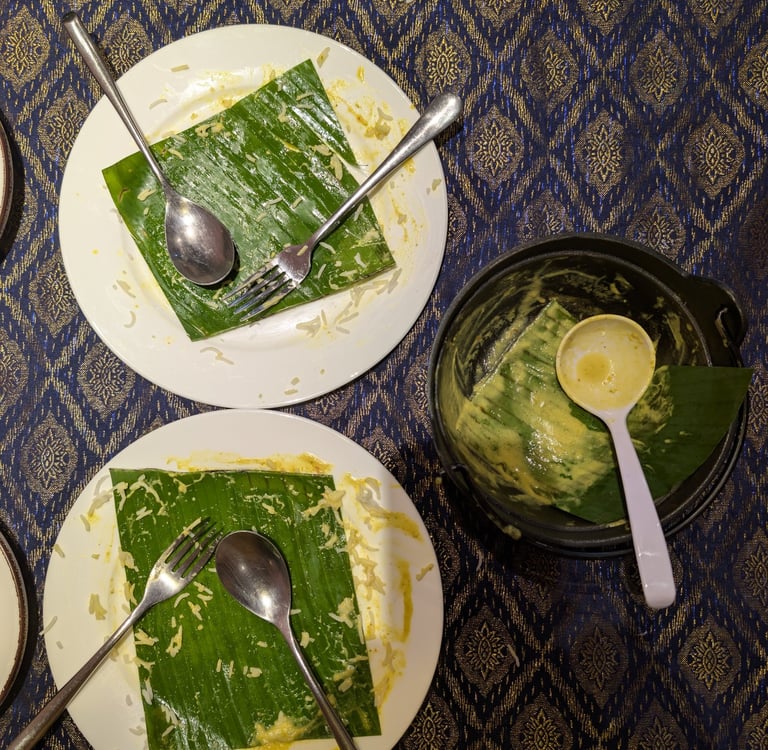 Empty plates with banana leaves and silver cutlery after a traditional Southeast Asian meal.