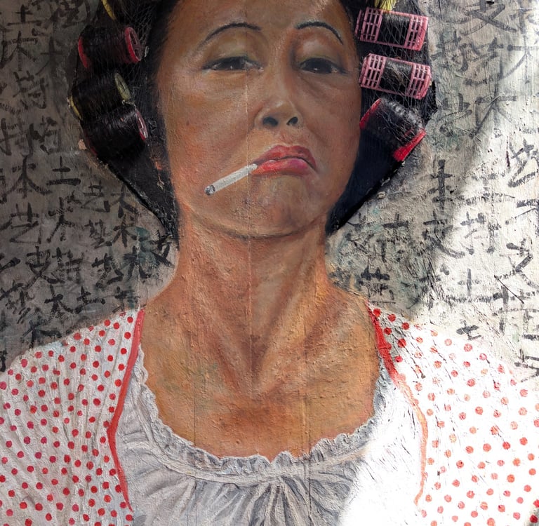 Street art mural of an Asian woman smoking a cigarette with hair rollers against a calligraphy background.