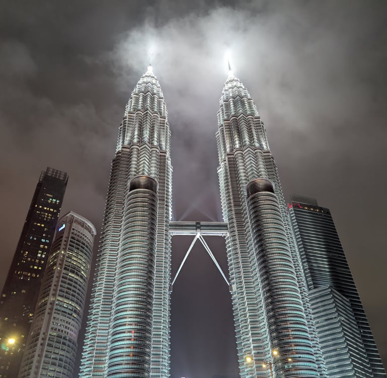 Illuminated Petronas Twin Towers in Kuala Lumpur, Malaysia, at night under a cloudy sky.