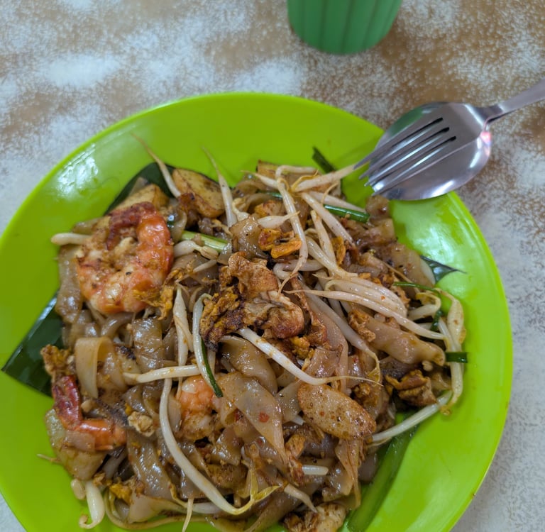 Authentic Char Kway Teow stir-fried rice noodles with prawns and bean sprouts on a green plate.