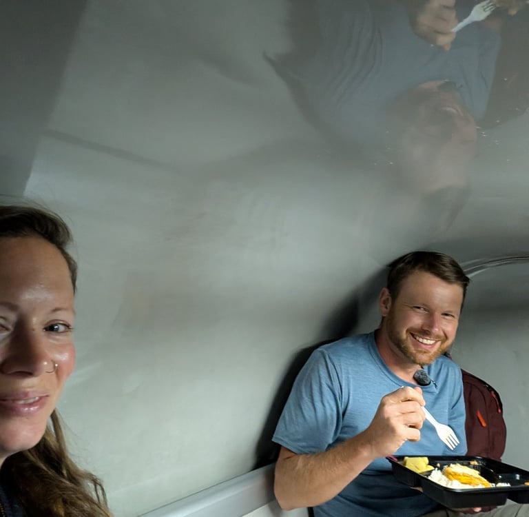 don and Samantha eating a meal inside a small train cabin while traveling.