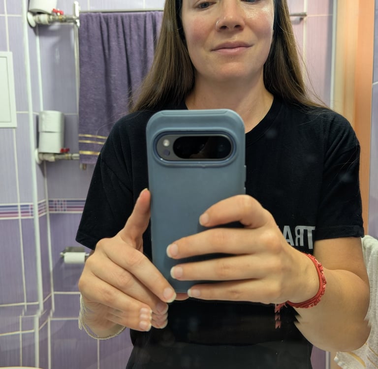 A woman with glowing skin taking a mirror selfie in a purple tiled bathroom after skincare 