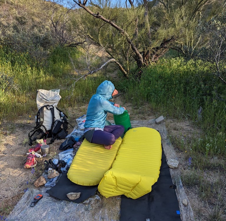 A woman inflating a yellow Therm-a-Rest Neoair sleeping pad in a lush desert canyon in Arizona.