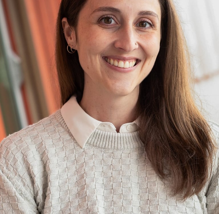A smiling woman with long brown hair smiling, wearing a cream sweater over a white collared shirt 
