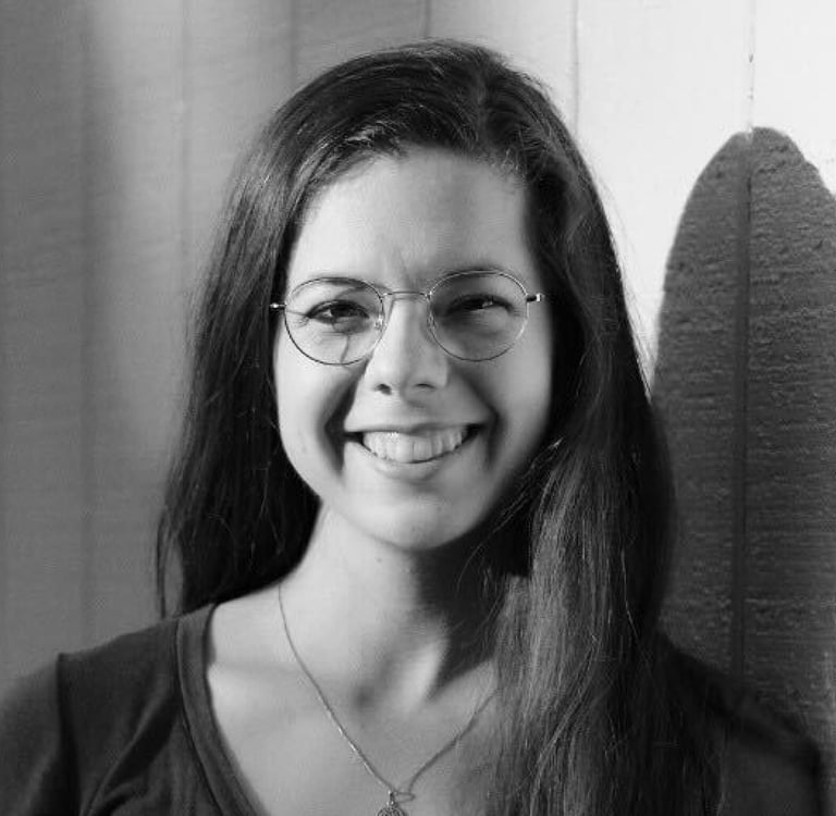 April Reissmann, a woman with glasses, wearing a v neck shirt and a necklace 