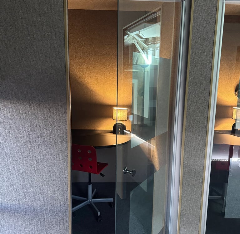 Deux cabines de bureau insonorisées avec portes vitrées, équipées d'un tabouret haut, tablette et lampe d'appoint.
