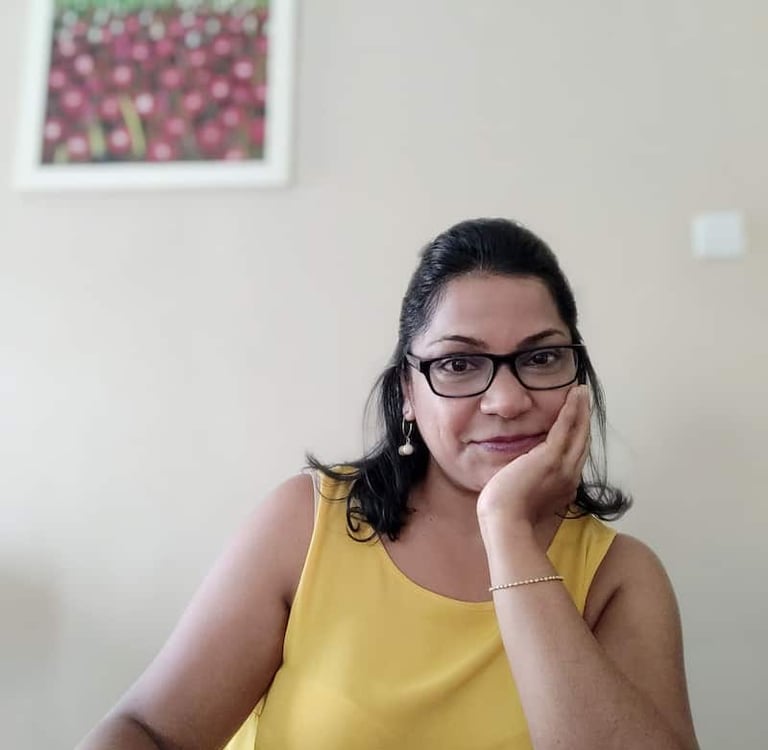girl in yellow top, glasses, hand on chin with a slow easy smile