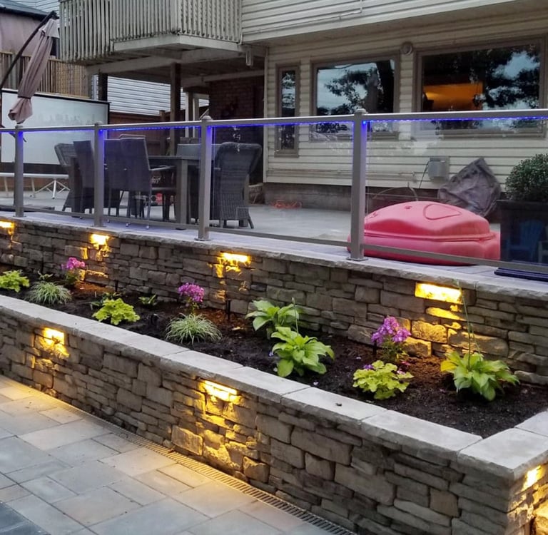 Modern stone retaining wall with integrated LED garden lighting and a glass deck railing.