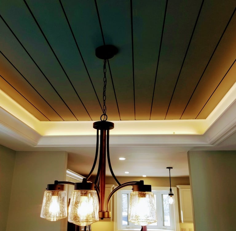 Modern bronze chandelier with seeded glass shades hanging from a tray ceiling with cove lighting.