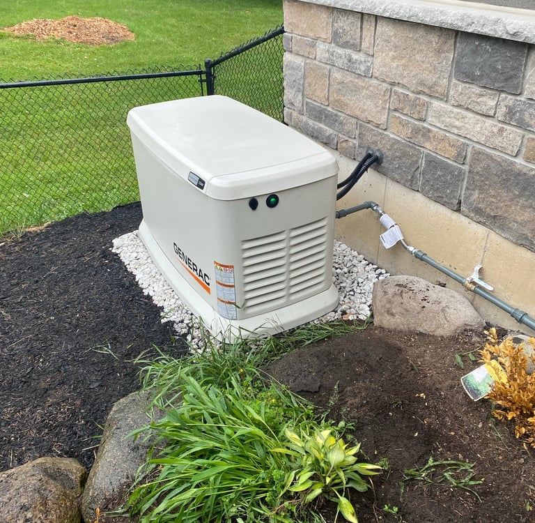 A tan Generac home standby generator installed on a gravel base next to a stone house foundation.