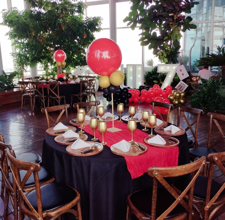 Elegant casino themed party table setting with gold goblets, red runner, and balloon centerpieces.