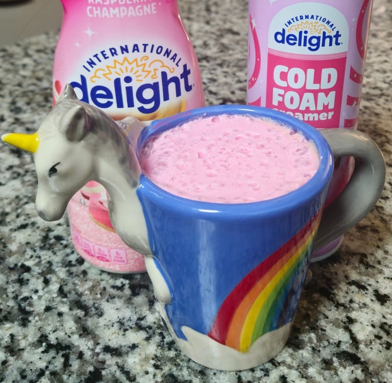 A picture a coffee mug shaped like a unicorn. Inside the mug shows pink cold foam.