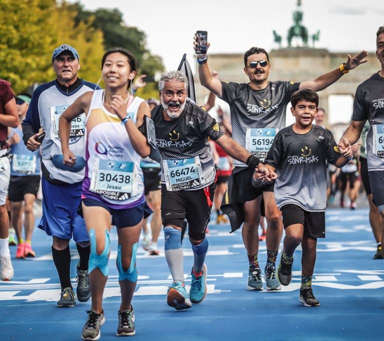 Cuatro corredores de Empujando Sonrisas corren eufóricos con la Puerta de Brandenburgo de fondo