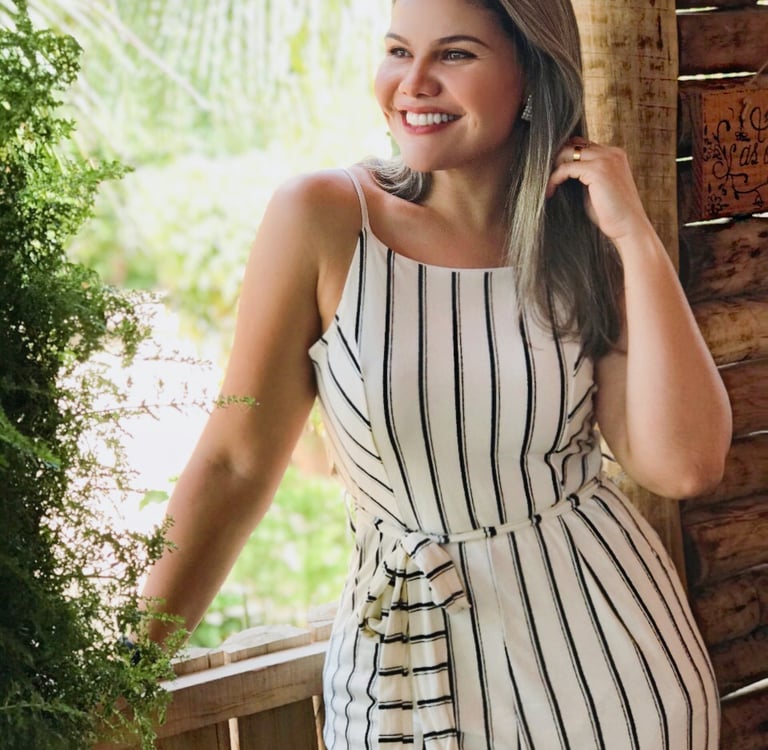 Priscila, Pri Cílios extensionista de cílios, sorrindo em fazenda com vestido branco.