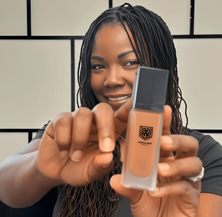 A woman holding a bottle of Yeshua Skin liquid foundation for dark skin tones.