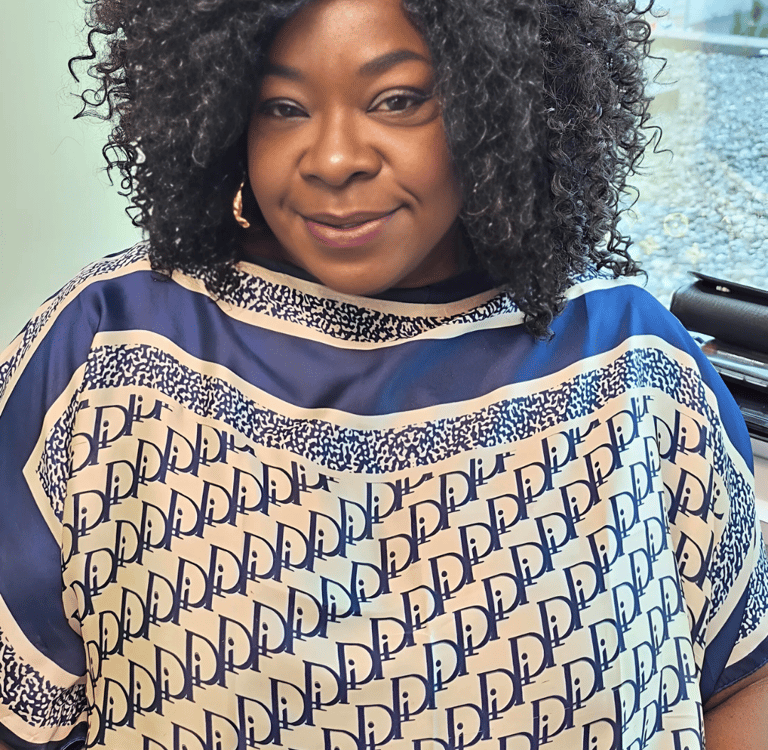 Smiling woman with voluminous curly hair wearing a blue and white patterned designer tunic top.