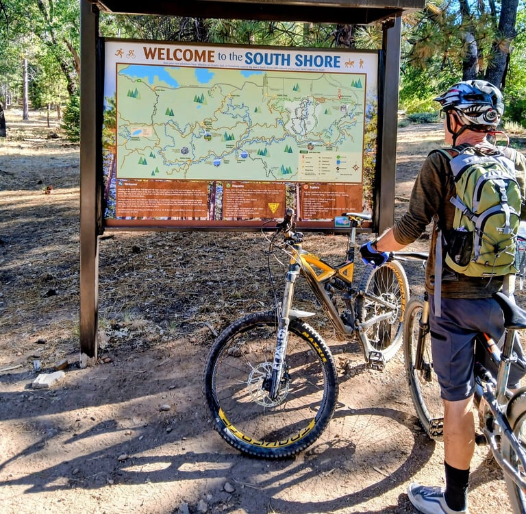 Mountain biker looking at trail map sign while wearing a hydration backpack for a long ride