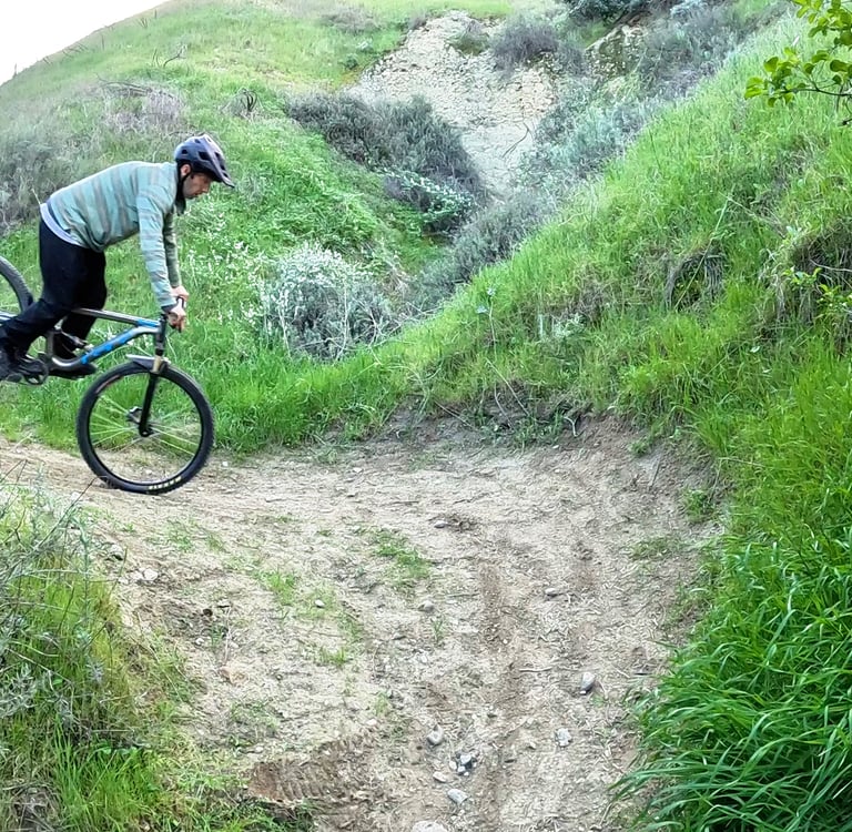 Rider modulating front brake to control rear wheel height during a stoppie pivot on a narrow trail