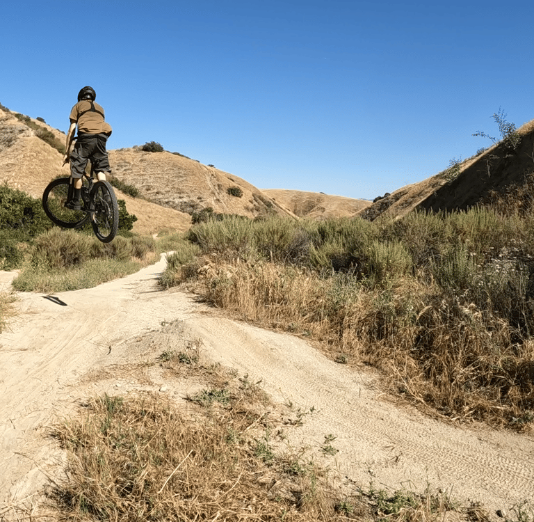 Mountain biker hitting a jump on a mountain bike trail at Hulda Crooks park in loma linda