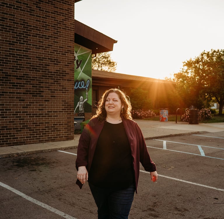 Smiling woman walking in a brick building parking lot at sunset with golden hour lighting.