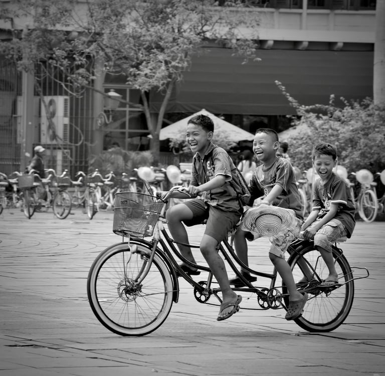 Three joyous youngs Indonesian boys on a bicycle riding in the main square of Kota Tua, Jakarta