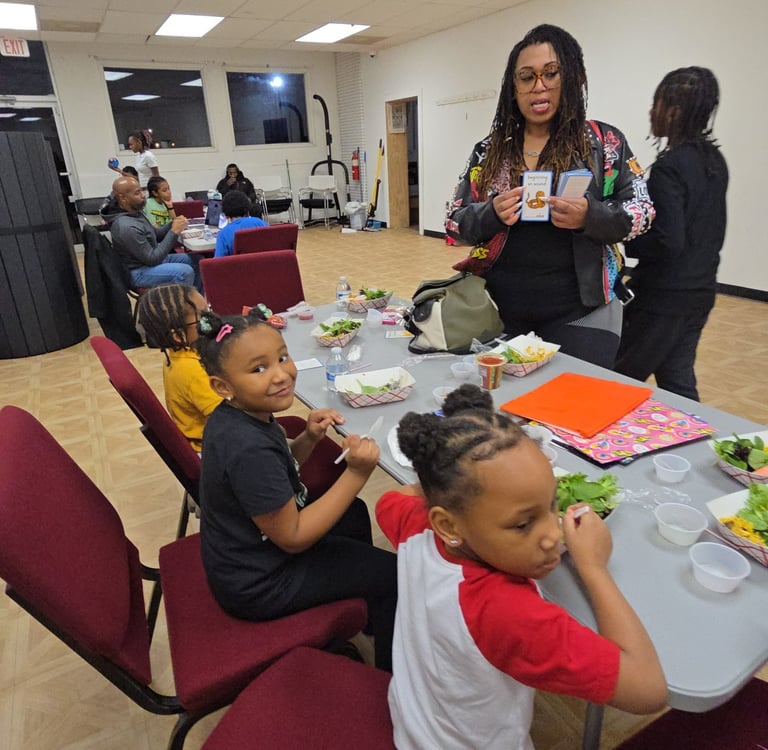 A group of children and adults participating in a community workshop with healthy meals and educational cards.