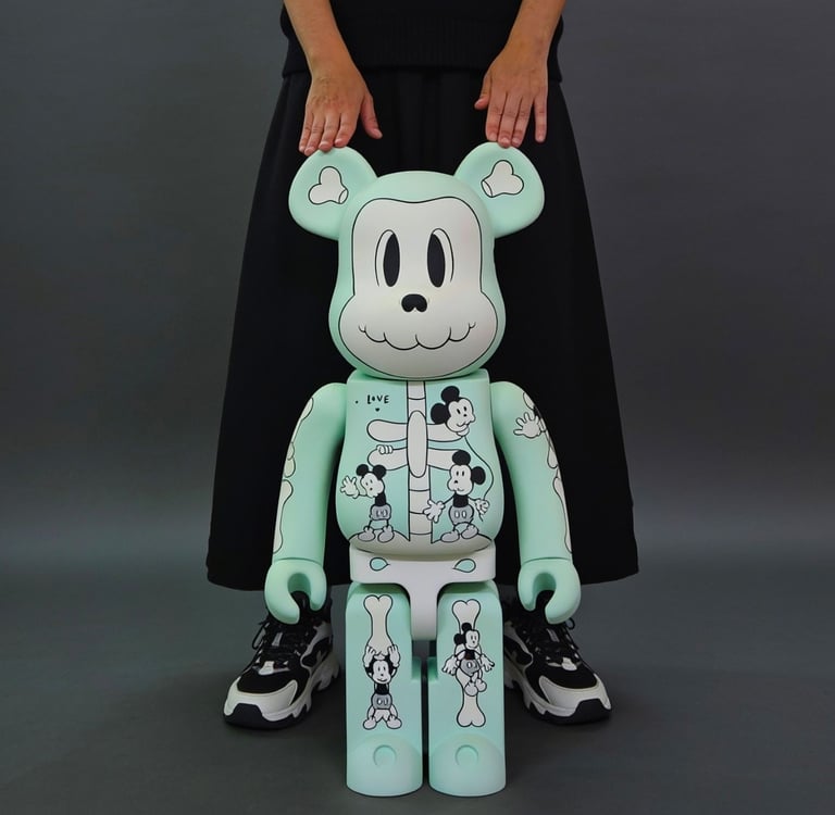 A mint green Bearbrick 1000% figure with Mickey Mouse skeleton graphics being held by a person.