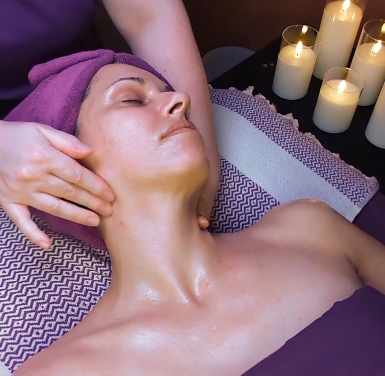 A woman receives a relaxing facial massage at a luxury spa with lit candles nearby.