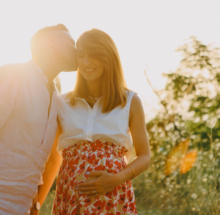 una donna incinta e un uomo che si baciano al tramonto