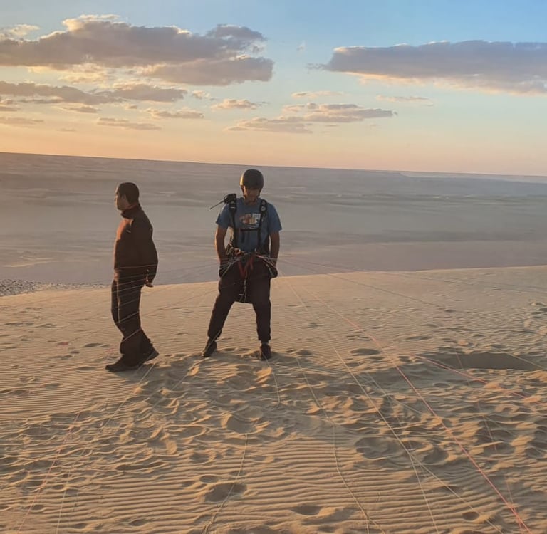 two people standing on a sand dune paragliding egypt