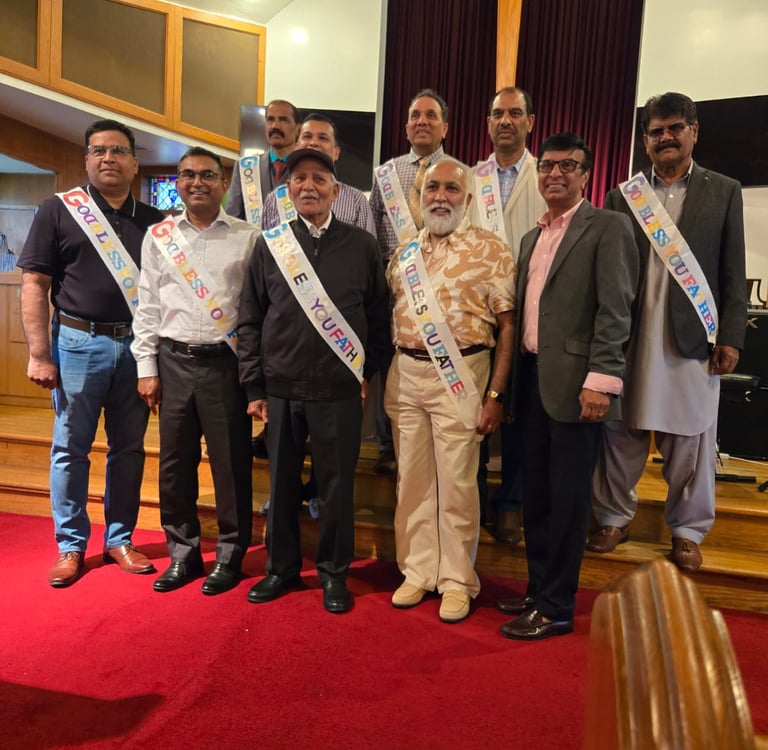 Nine South Asian fathers and father-figures wearing celebratory sashes, standing and smiling under a