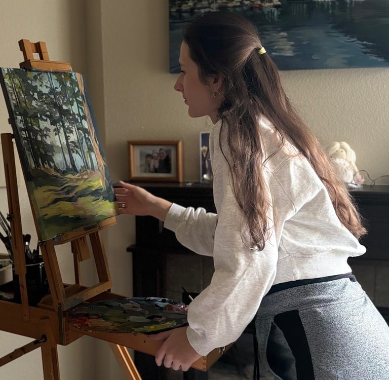 Angela Moiseieva painting at her easel in a bright art studio.
