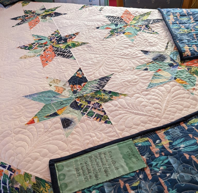 a white quilt with colorful stars and ornate quilting and a hand-lettered label