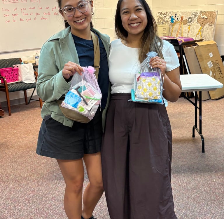 two women standing next to each other in a room holding hygiene kits
