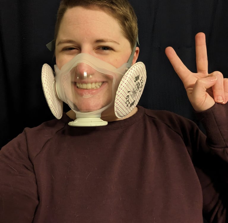 Melody throws a peace sign. She's wearing a transparent mask.