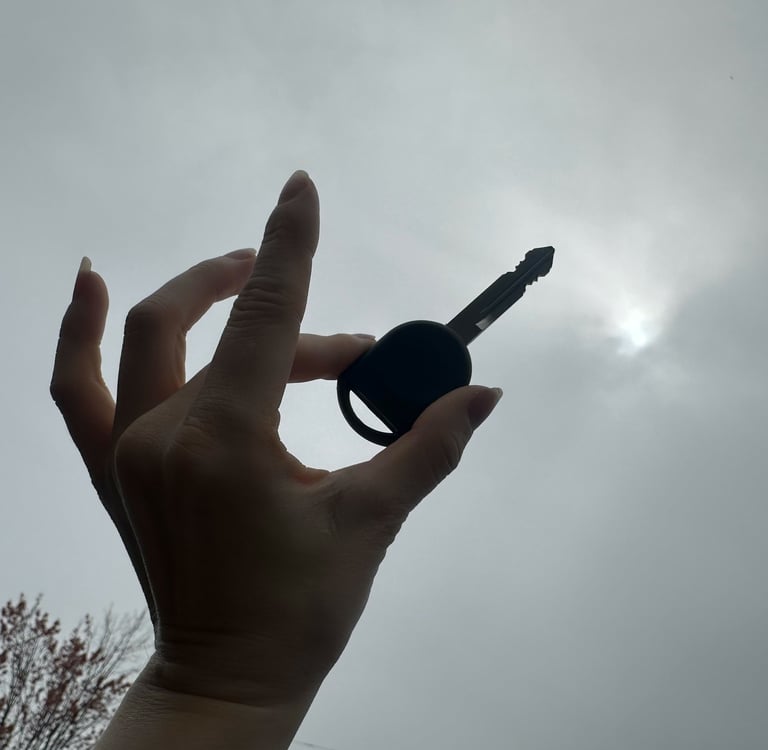 A hand holding a key silhouette against a cloudy sky