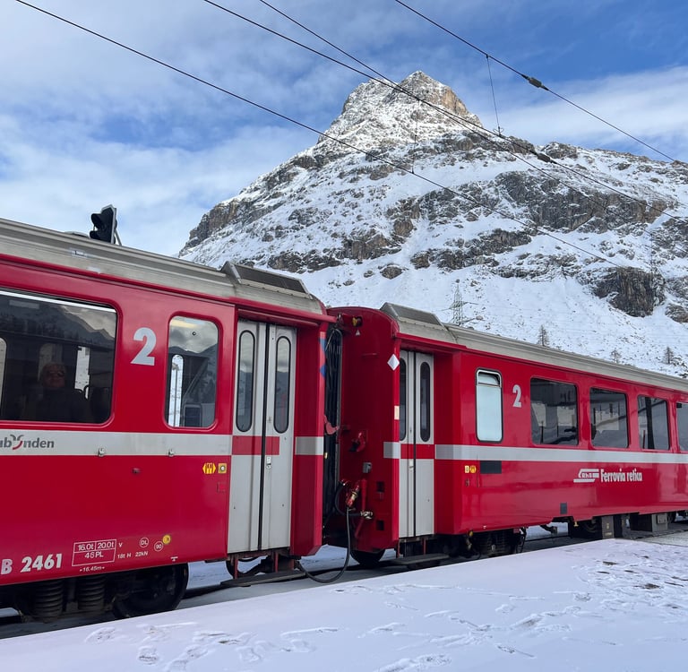 Two red Rhaetian Railway train cars in front of the mountains at Bernina Pass in Switzerland