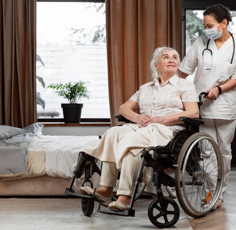 A female nurse in a face mask assisting a senior woman in a wheelchair during home health care.