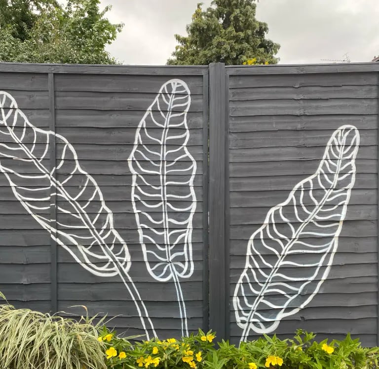 Modern graphic mural of three large tropical leaves on grey yard fence with flowers, by House of Lyr