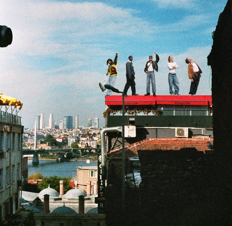 A group of diverse friends in casual fashion posing on an urban rooftop overlooking a scenic city skyline.