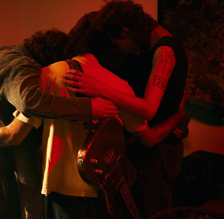 Band members in a huddle with an electric guitar under moody red stage lighting.
