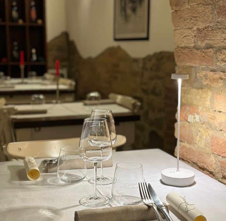 Tavola apparecchiata con calici di vino in sala con mattoni a vista - Cozy indoor table setting and 