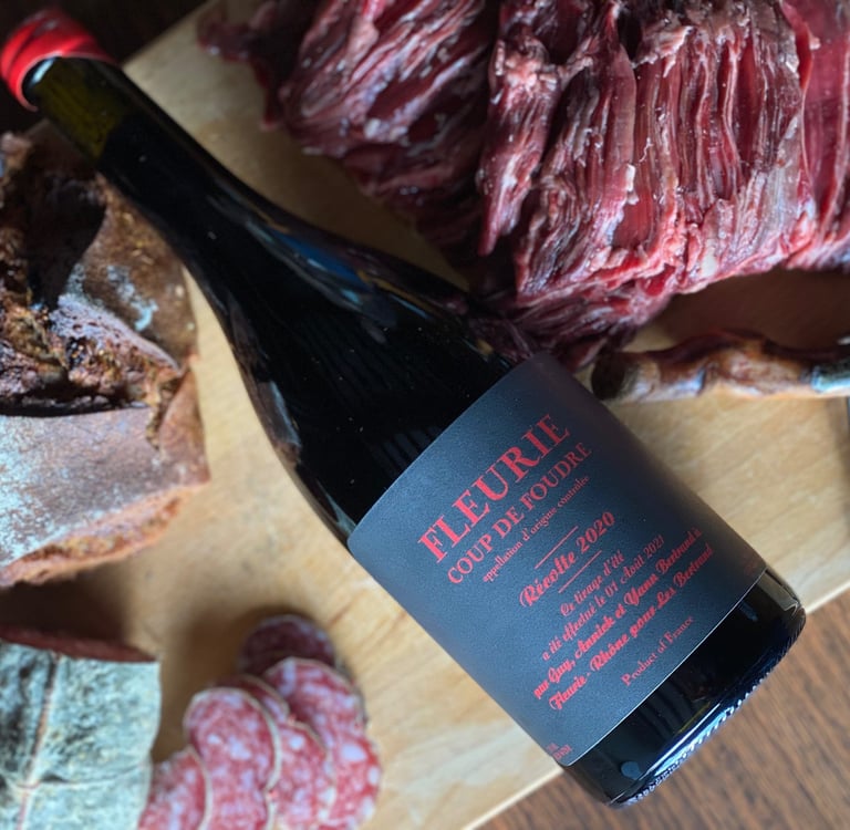 Une bouteille de vin rouge, du pain, de la viande et du saucisson sur une planche en bois.