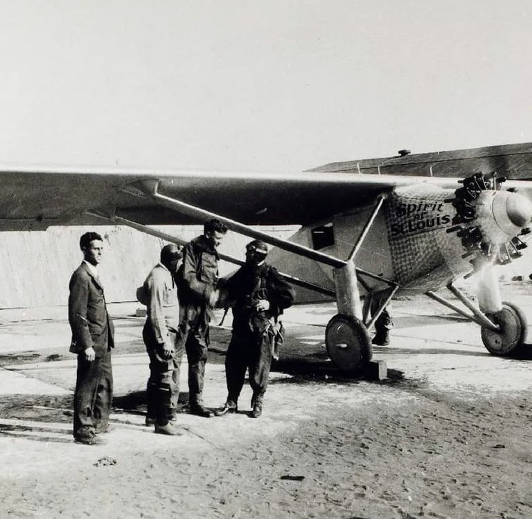 Charles Lindbergh and crew stand beside the historic Spirit of St. Louis aircraft on a runway.