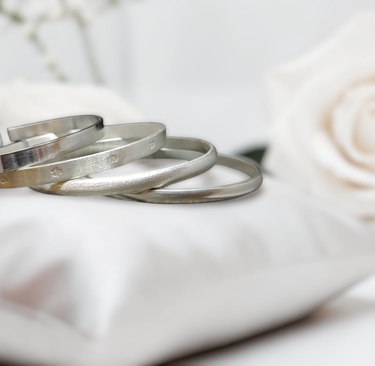Elegant stack of 999 fine silver bangles on a white satin pillow with roses.