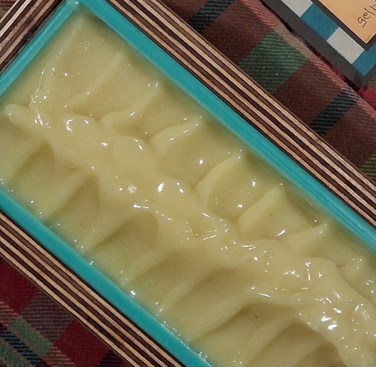 Freshly poured yellow handmade soap batter in a silicone loaf mold with a wooden frame.