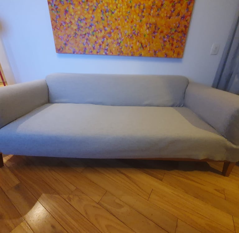 Um sofá moderno de tecido cinza com pernas de madeira em um piso de madeira abaixo de uma pintura ab