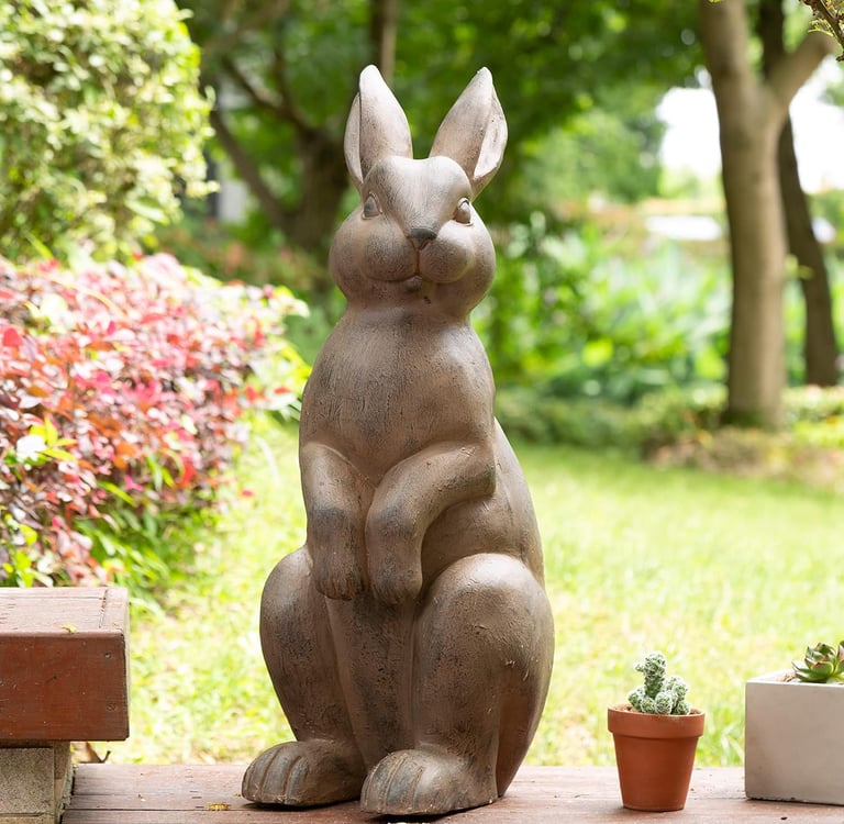 Decorative stone rabbit statue standing in a lush green garden setting.